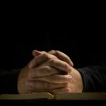 Mãos postas em oração sobre a Bíblia, ilustrando a confiança em Deus e a paz que guarda o coração conforme Filipenses 4.6-7.